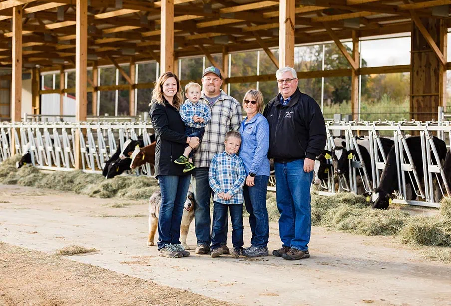 Family visiting dairy farm with Holstein cows inside a modern barn, showcasing sustainable foodservice and dairy products from Burnett Dairy Cooperative, celebrating local dairy farming and community.