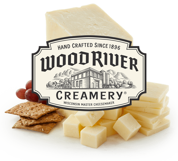Cheddar cheese block with cheese cubes, crackers, and grapes on a white plate, showcasing Wood River Creamery's handcrafted Wisconsin cheese products.